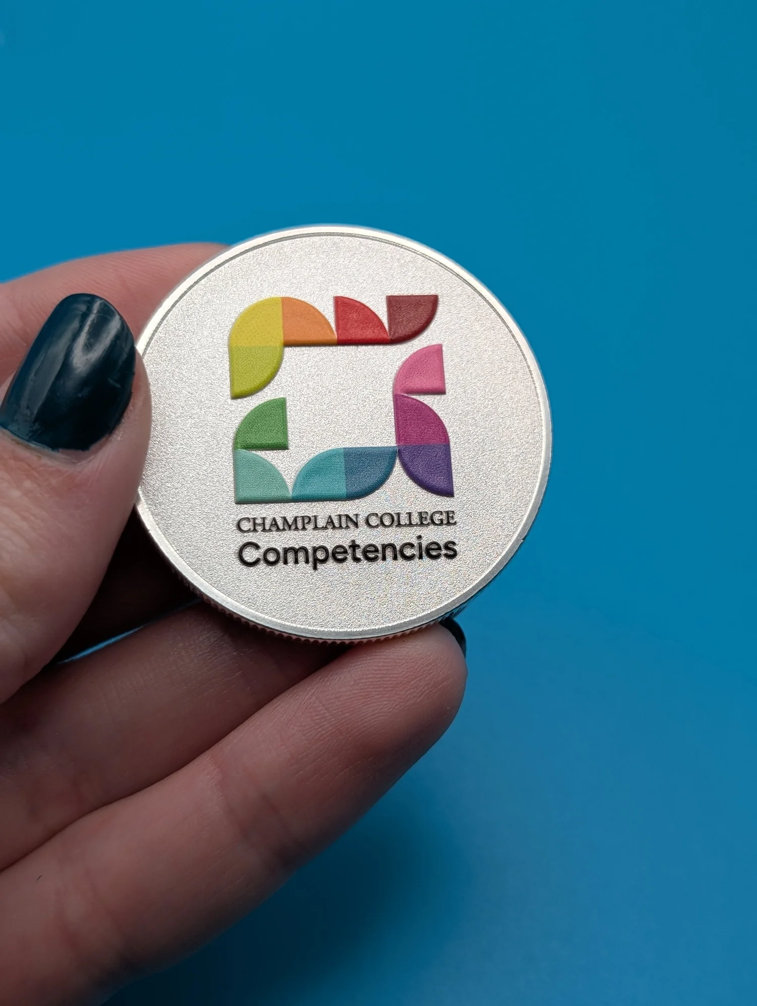 A UV-printed metal coin with a full-color logo mark, held in hand.